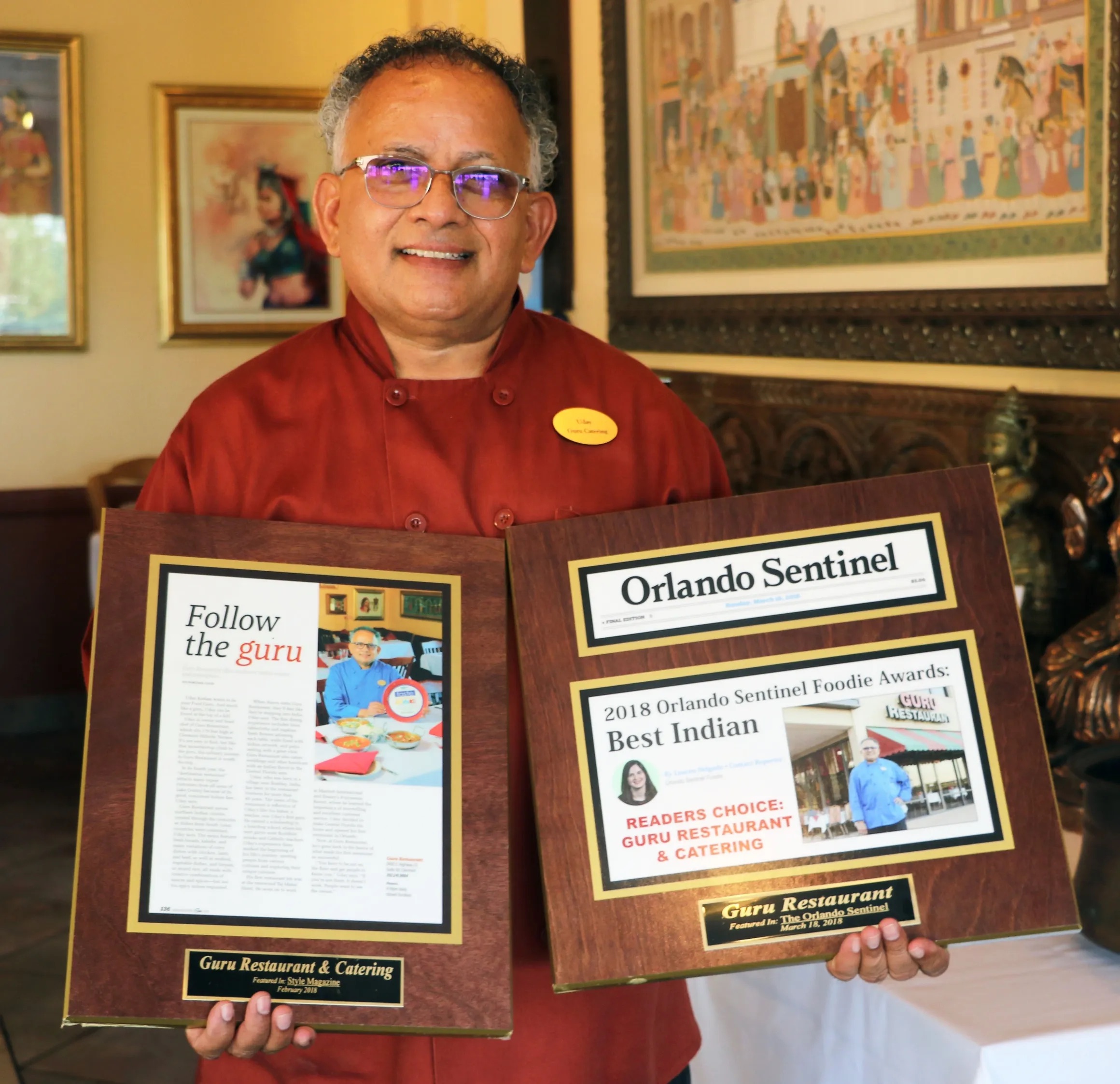 Chef Uday standing and holding more awards that he received for his restaurant Guru